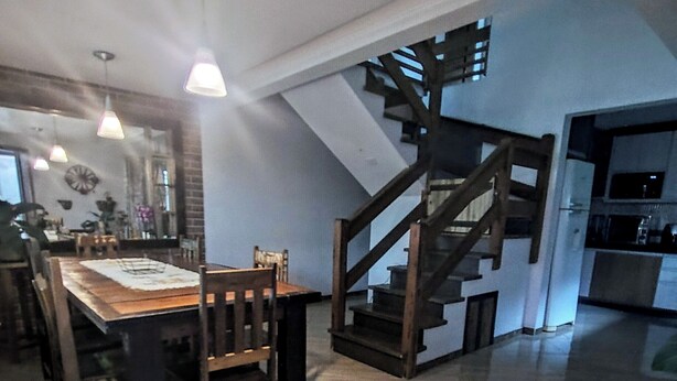Un comedor amplio con una mesa y sillas de madera, una escalera y una cocina al fondo.