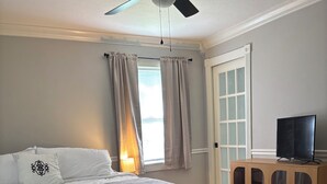 A bedroom with a bed, a ceiling fan, a wooden cabinet, and a window with curtains. - A peaceful 3-bedroom house in beautiful downtown Rogers (Rogers)