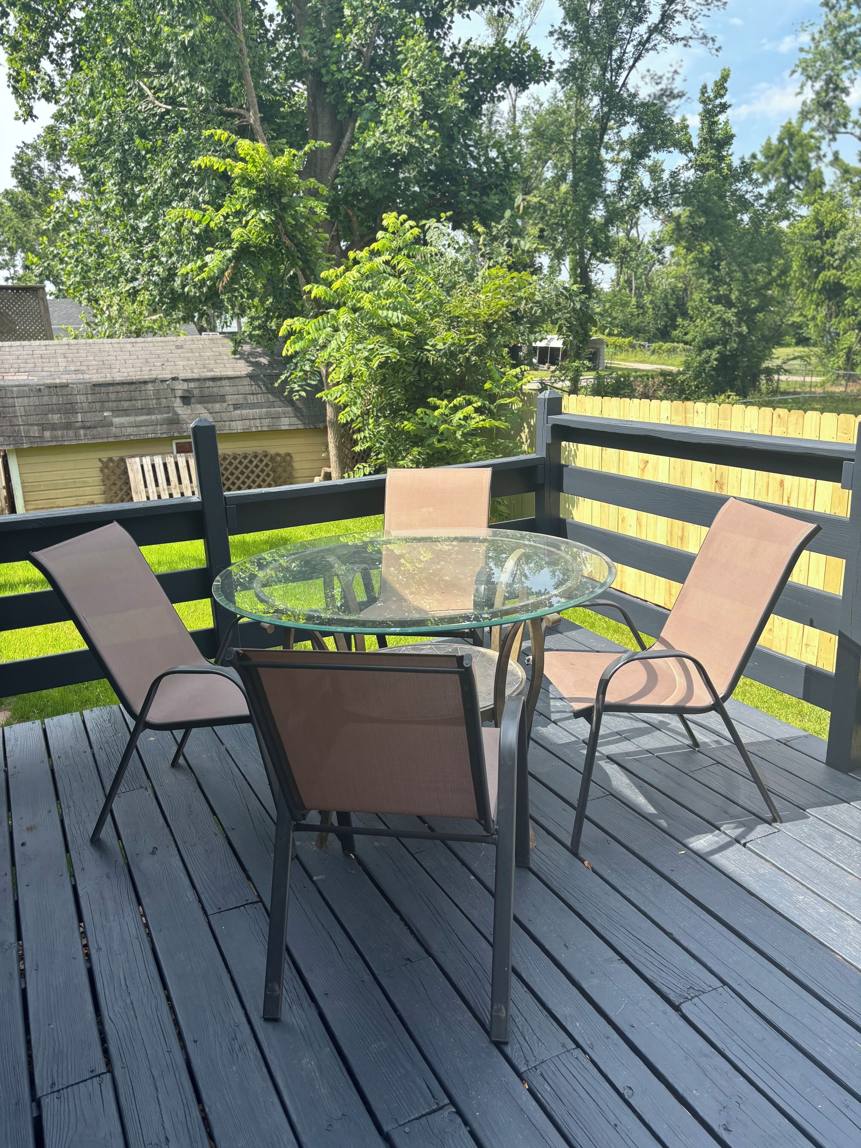 Mesa con cubierta de vidrio y cuatro sillas sobre una terraza de madera.