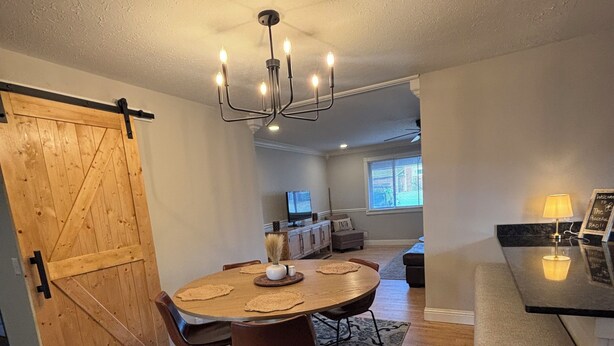 A dining area with a wooden table, chairs, and a chandelier. There is a sliding barn door, a rug, and a bench. - A peaceful 3-bedroom house in beautiful downtown Rogers (Rogers)