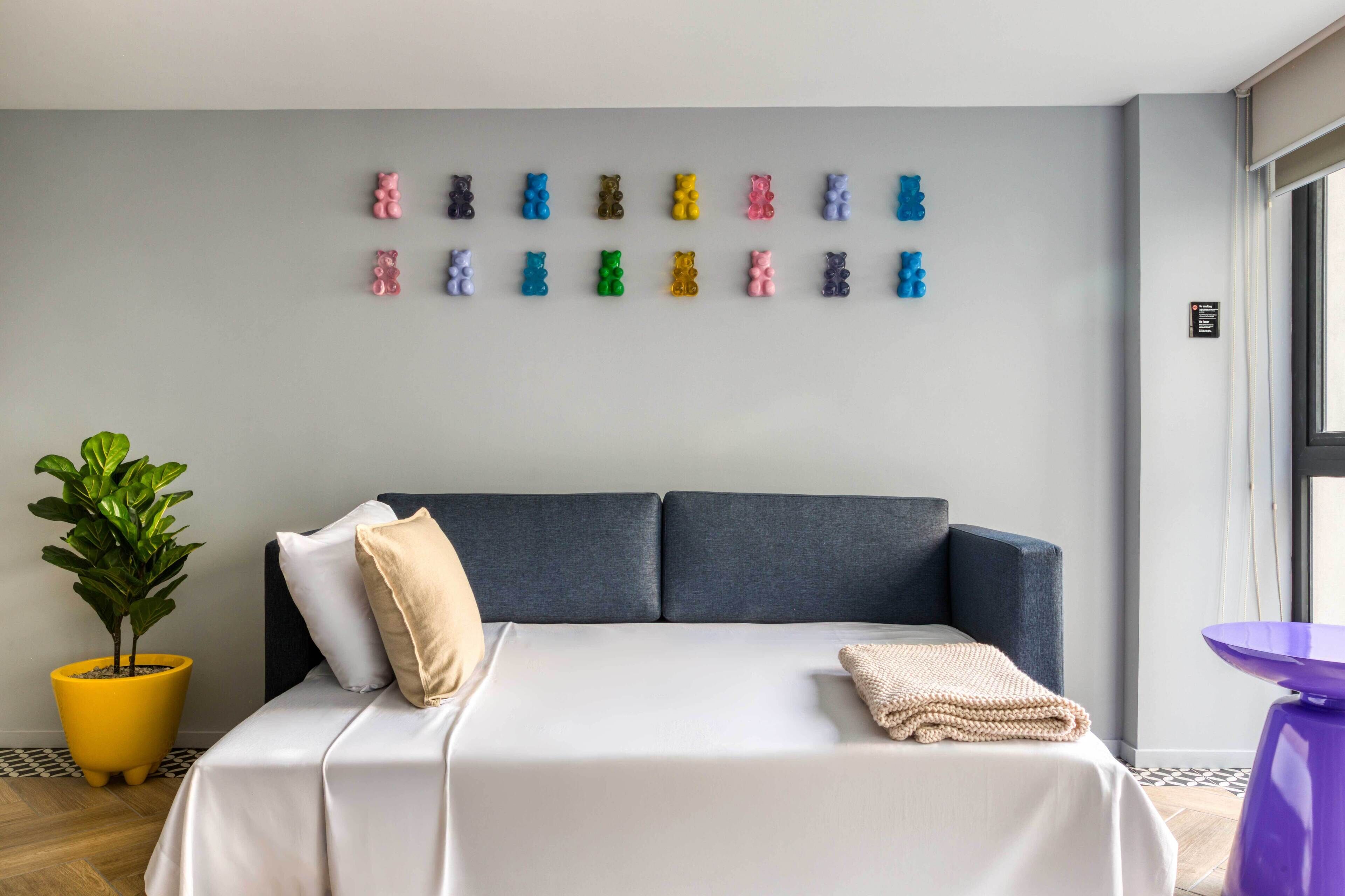 A modern hotel room with a large bed, a potted plant, and a wall decorated with colorful bear figurines.