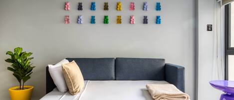 A modern hotel room with a large bed, a potted plant, and a wall decorated with colorful bear figurines.