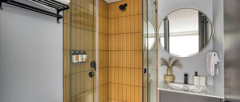 A modern bathroom with a glass shower enclosure, a white sink, and a round mirror.