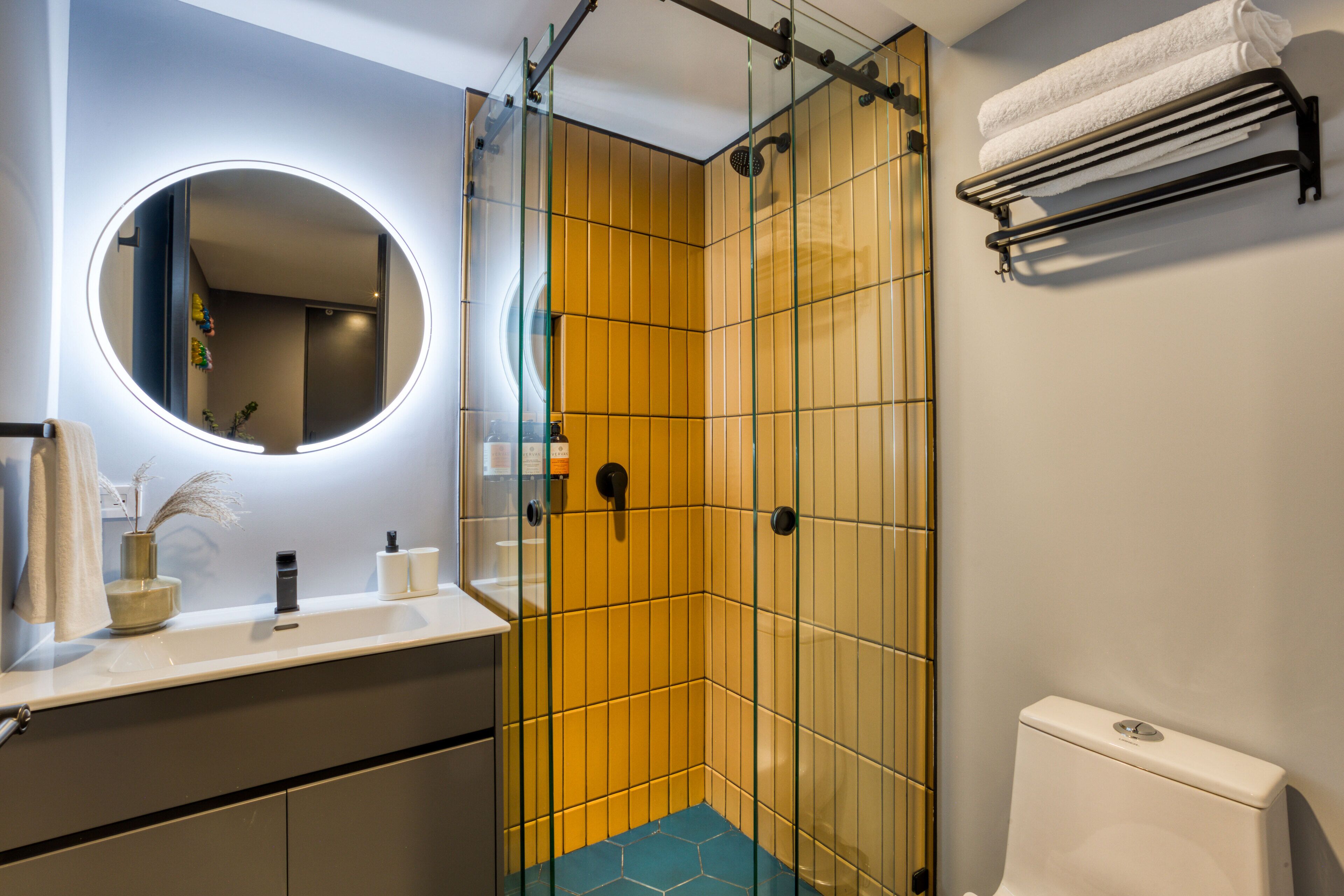 A bathroom with a glass-enclosed shower, a round mirror, a white sink, and a towel rack.