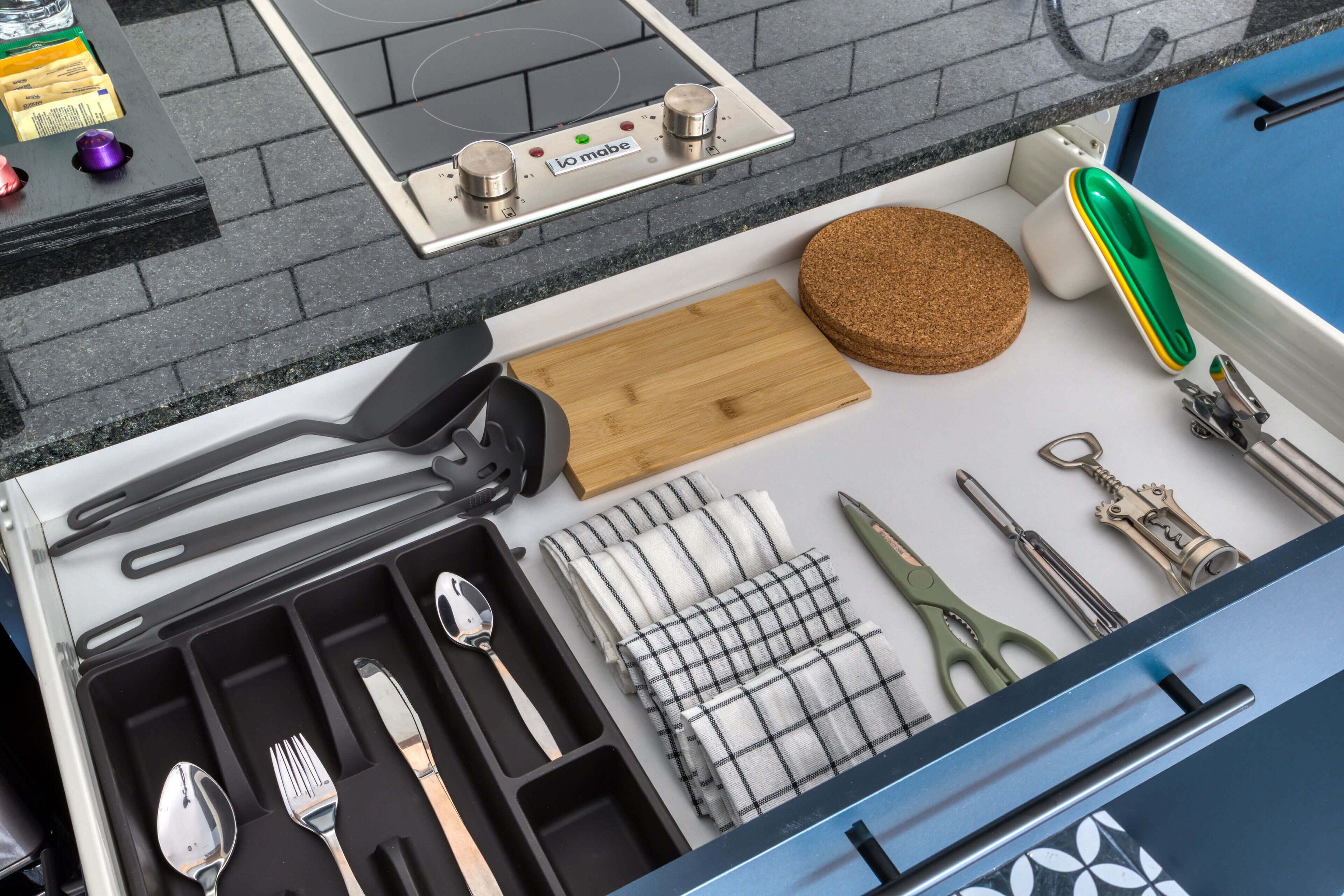 A kitchen with a built-in stove, a cutting board, a cork mat, and various utensils.