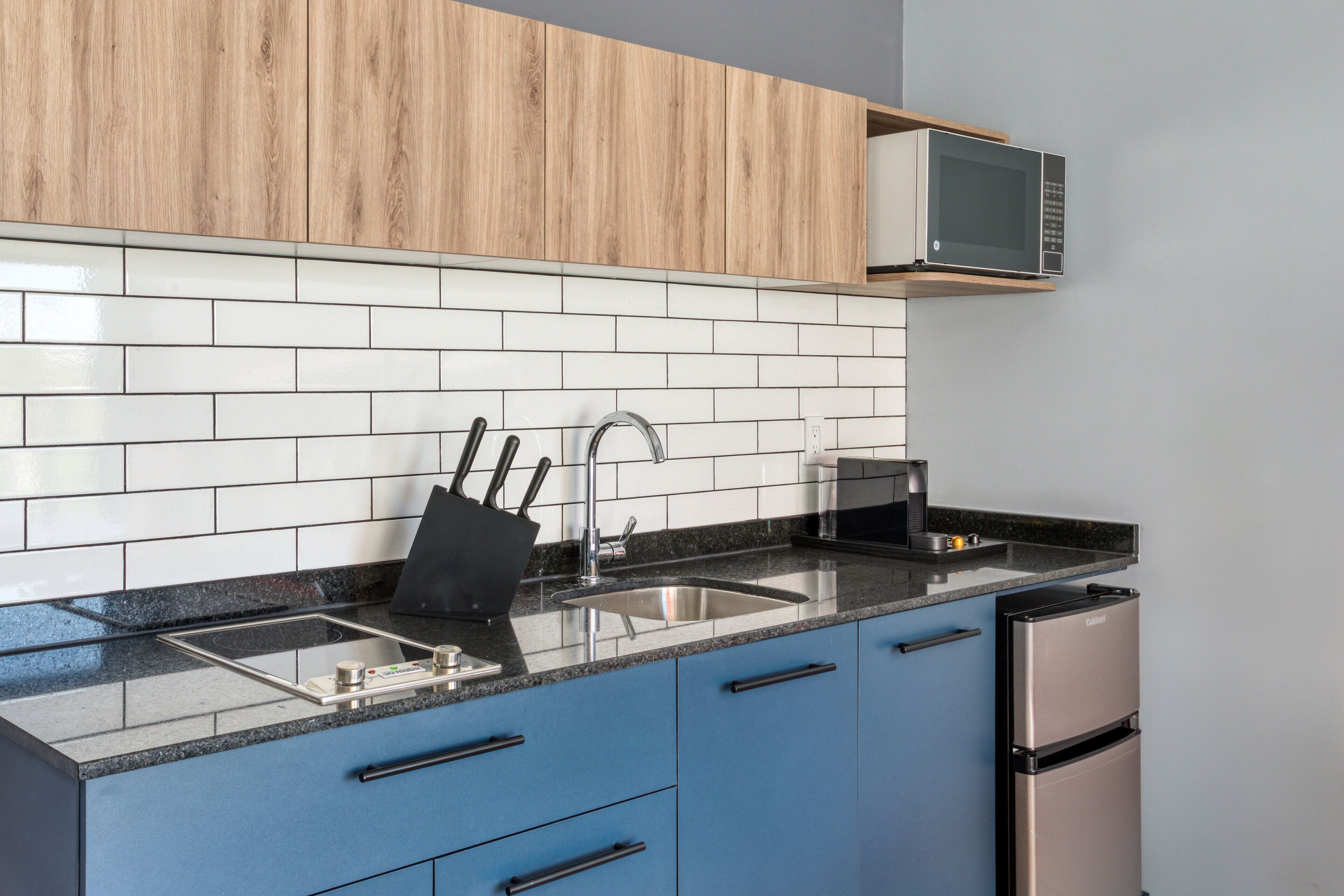 A modern kitchen with a black countertop, stainless steel appliances, and blue cabinets.