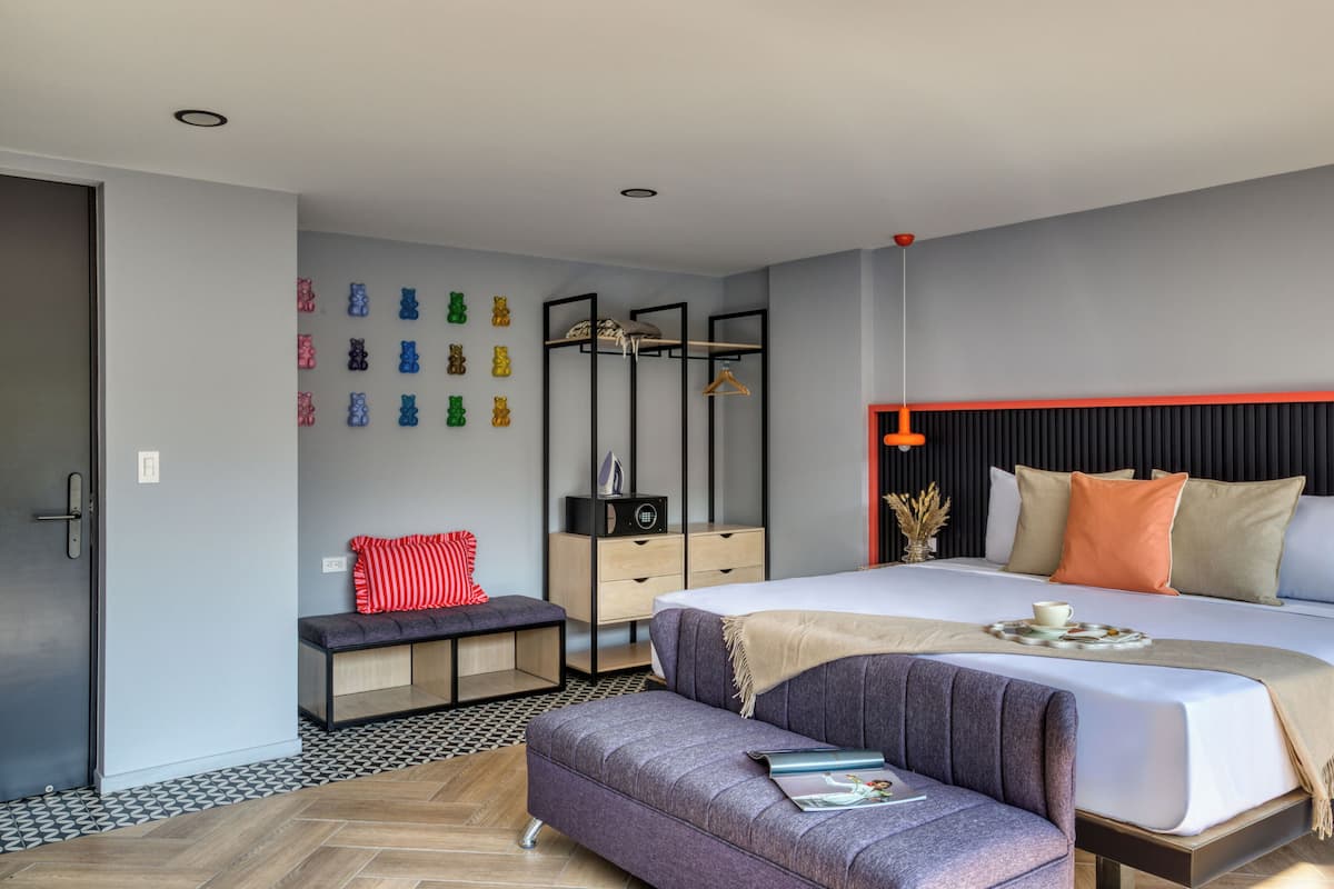 A modern bedroom with a large bed, a bench, a dresser, and a wall-mounted coat rack.