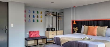 A modern bedroom with a large bed, a bench, a dresser, and a wall-mounted coat rack.
