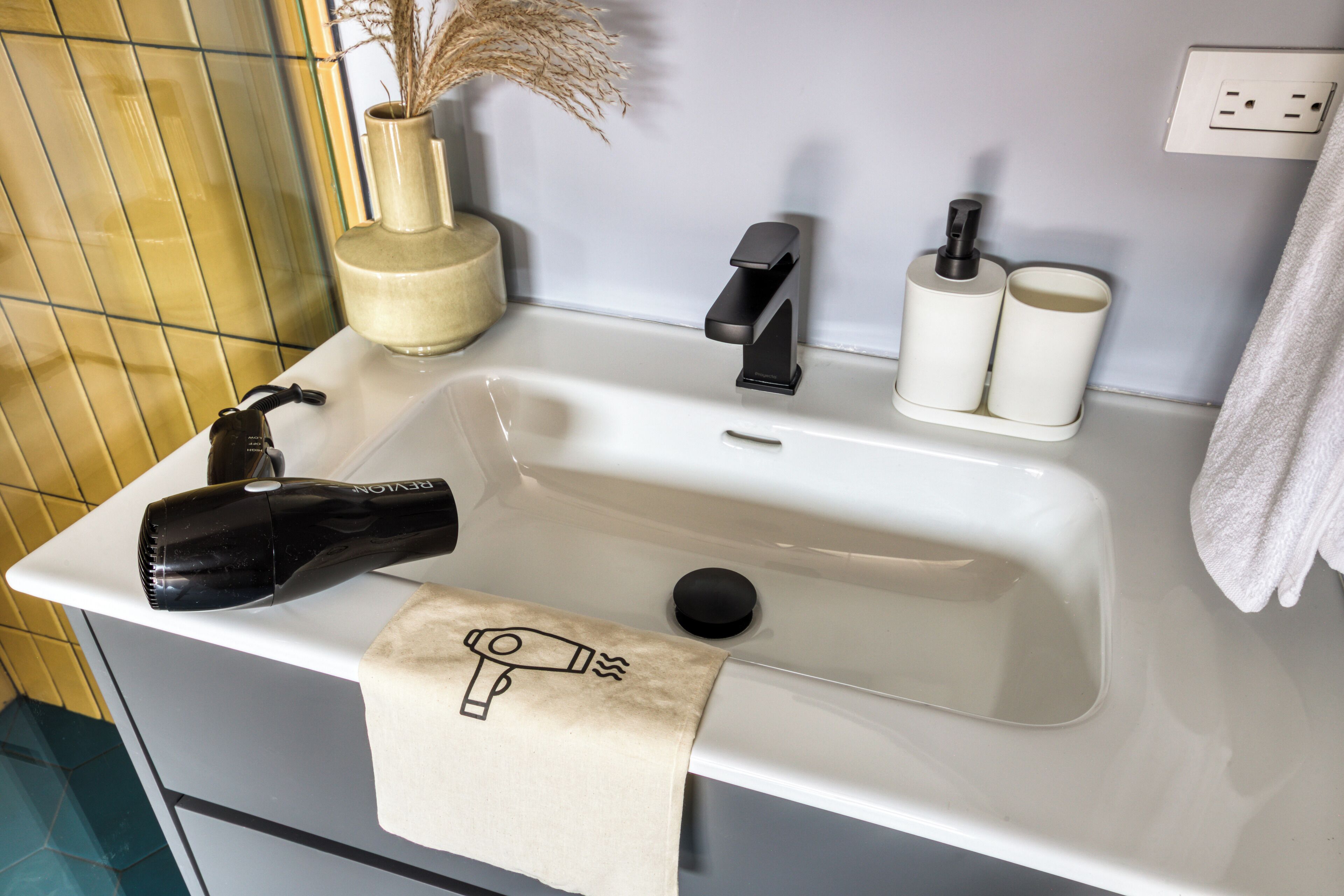 Ein Waschbecken mit Fön, Handtuch und einer Vase mit Trockenblumen.