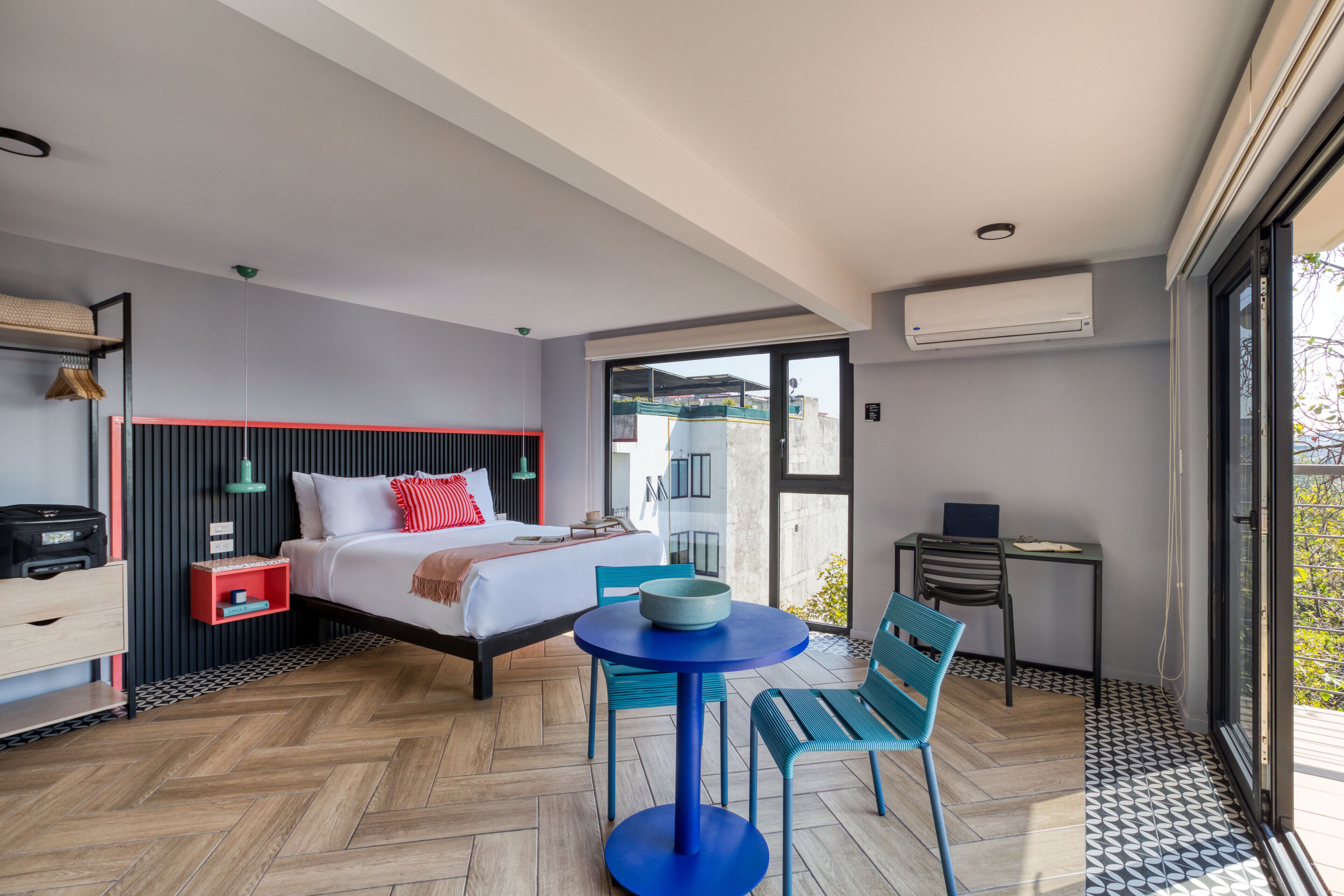 A modern hotel room with a large bed, a small table, two chairs, a desk, and a balcony with a view.