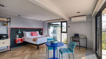A modern hotel room with a large bed, a small table, two chairs, a desk, and a balcony with a view.
