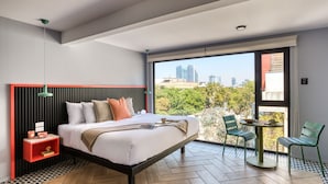 A modern bedroom with a city view, a wooden floor, a bed with pillows, a nightstand, and a small table with chairs. - ULIV Condesa (Mexico City)