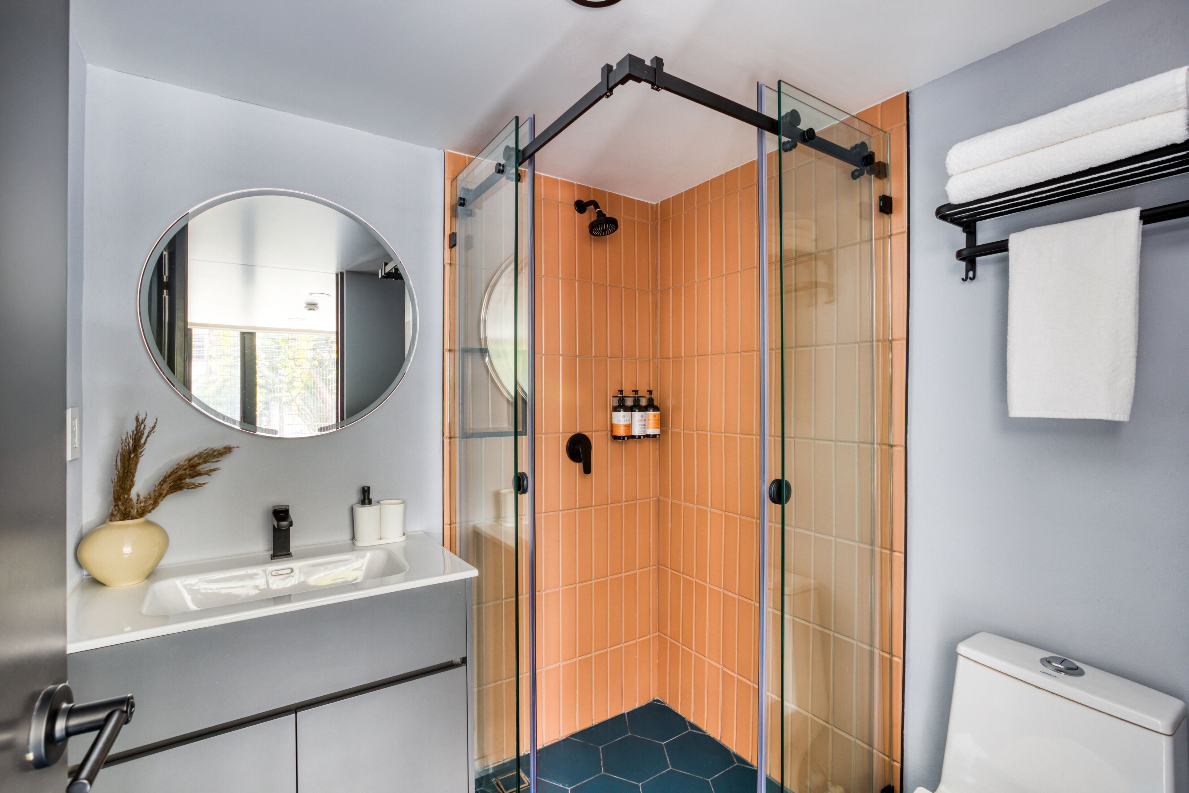 A modern bathroom with a glass-enclosed shower, a round mirror, a white sink, and a toilet.