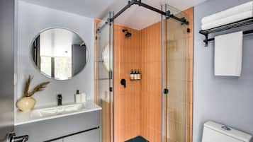 A modern bathroom with a glass-enclosed shower, a round mirror, a white sink, and a toilet.