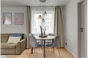 A modern living room with a beige sofa, a round dining table with four chairs, and a large window with sheer curtains. - Beautiful 2-bedroom apartment in charming Gdańsk in the old town (Gdańsk)