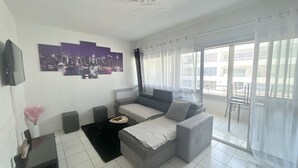 Una sala de estar moderna con un sofá gris, una mesa de centro negra y una obra de arte con un paisaje urbano en la pared.