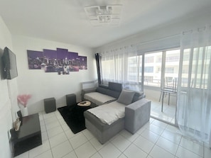 A modern living room with a grey sofa, a black coffee table, and a cityscape artwork on the wall. - Family apartment near beach with shared pool (Le Barcarès)