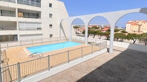 Un edificio moderno con zona de piscina, que incluye una piscina cercada y un área de estar cubierta.