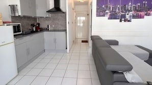 Una cocina moderna con armarios blancos, una campana extractora negra y un microondas. Hay un sofá gris y un cuadro grande con una vista urbana.