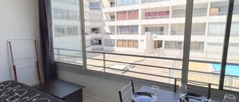 A modern hotel room with a large window offering a view of a pool and a multi-story building.