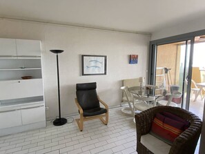 A living room with a black leather chair, a wicker sofa, a glass table, and a white cabinet. - Modern T2 in Canet Beach - 4 pers, sea view balcony (Canet-Plage)