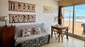 A room with a sofa, a small table, and a chair. There are wall art pieces depicting ancient Egyptian scenes. - Pleasant studio with terrace, beach access, private parking (Le Barcarès)