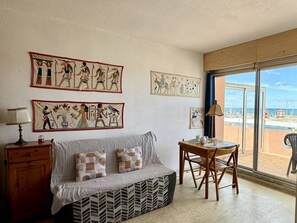 A room with a sofa, a small table, and a chair. There are wall art pieces depicting ancient Egyptian scenes. - Pleasant studio with terrace, beach access, private parking (Le Barcarès)