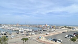 A marina with boats and cars, a clear sky, and a road leading to the marina. - Pleasant studio with terrace, beach access, private parking (Le Barcarès)