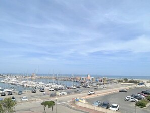 A marina with boats and cars, a clear sky, and a road leading to the marina. - Pleasant studio with terrace, beach access, private parking (Le Barcarès)