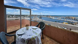 A balcony with a table set for dining, overlooking a marina with boats and a cityscape. - Pleasant studio with terrace, beach access, private parking (Le Barcarès)