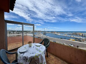 A balcony with a table set for dining, overlooking a marina with boats and a cityscape. - Pleasant studio with terrace, beach access, private parking (Le Barcarès)
