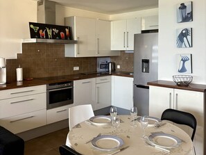 A modern kitchen with white cabinets, a stainless steel refrigerator, and a dining table set for four. - Seaside apartment with terrace and secure parking (Le Barcarès)