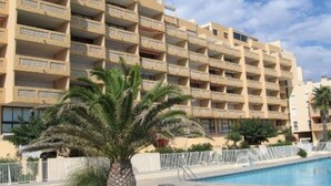 A multi-story hotel with balconies, a swimming pool, and palm trees. - Seaside apartment with terrace and secure parking (Le Barcarès)