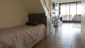 A bedroom with a bed, a staircase, a kitchen area, and a dining area with a chair. - Seaside apartment with terrace and secure parking (Le Barcarès)