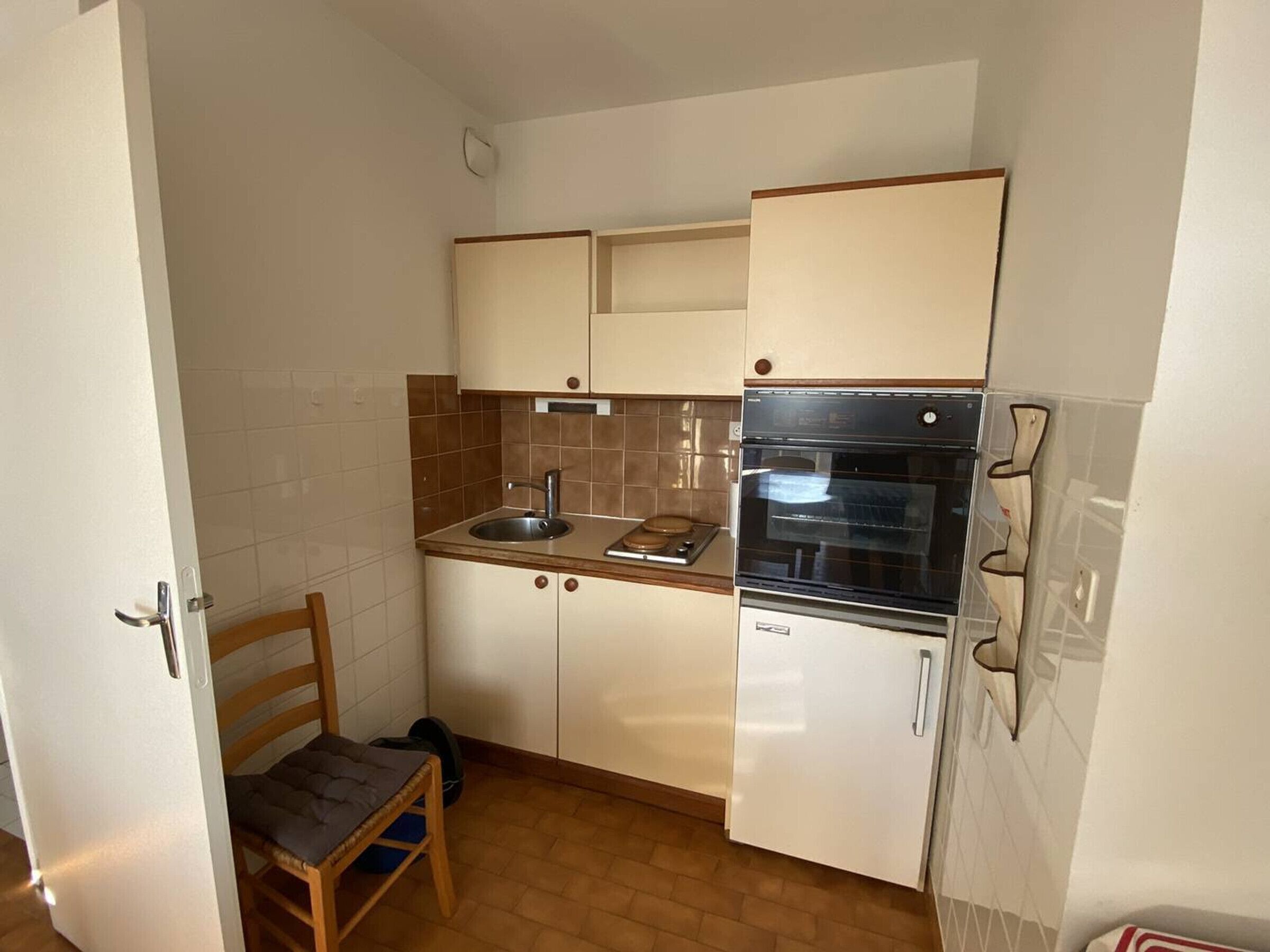 Een kleine keuken met een spoelbak, fornuis, oven en een stoel.