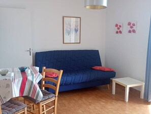 A living room with a blue sofa, a dining table with chairs, a small white table, and a framed picture on the wall. - 2-room south-facing, terrace, 4 pers, beachfront (Canet-Plage)