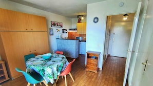 Kompakti oleskelutila, jossa on ruokailualue, pieni keittiö ja pieni puinen kaappi.