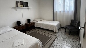 A hotel room with two beds, a chair, a desk with a lamp, a shelf with a picture, and a window with curtains. - 2-Bedroom Flat, 50m from the beach, near center (Canet-en-Roussillon)
