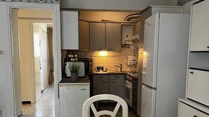 A compact kitchen with a dining area, featuring a refrigerator, stove, sink, and a small countertop with a potted plant. - 2-Bedroom Flat, 50m from the beach, near center (Canet-en-Roussillon)