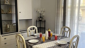 A dining area with a table set for four, a cabinet with decorative items, and a view of the outside through sheer curtains. - 2-Bedroom Flat, 50m from the beach, near center (Canet-en-Roussillon)