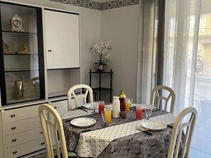 A dining area with a table set for four, a cabinet with decorative items, and a view of the outside through sheer curtains. - 2-Bedroom Flat, 50m from the beach, near center (Canet-en-Roussillon)