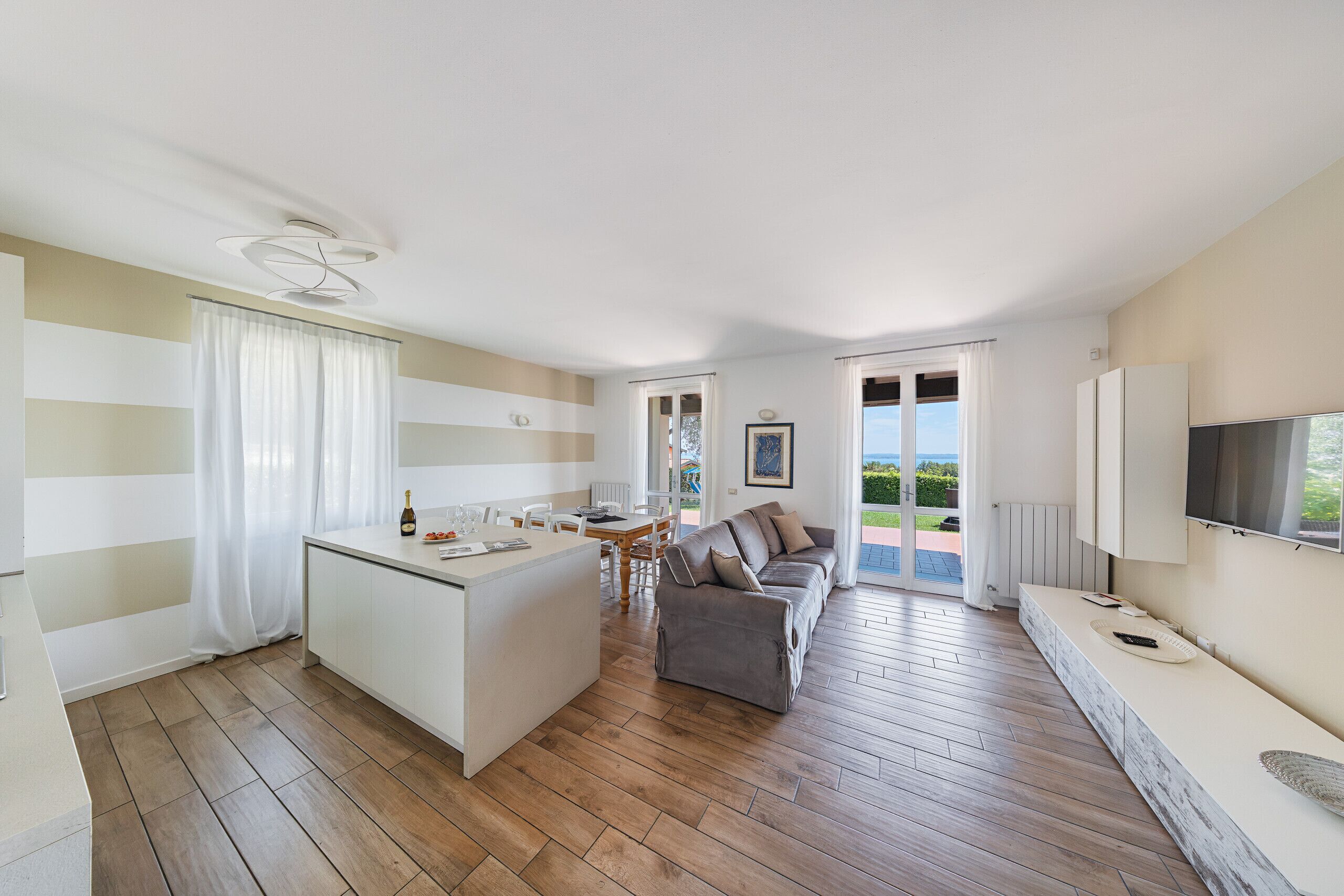 Eine moderne Küche mit Kochinsel, Essbereich mit Tisch und Stühlen, eine Couch und ein an der Wand befestigter Fernseher.