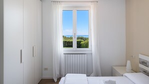 Une chambre à coucher comprenant un lit, une table de chevet, une fenêtre donnant sur un paysage verdoyant et aquatique, et un radiateur.