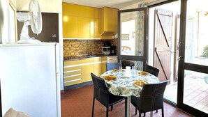 Une cuisine de taille réduite avec des meubles de couleur jaune, un réfrigérateur blanc et une table à manger pour quatre personnes.