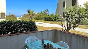 Un balcon avec une table dressée pour deux personnes, une vue sur la mer et un bâtiment en arrière-plan.