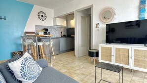 Ein modernes Wohnzimmer mit einem grauen Sofa, einem Fernseher und einer Küche im Hintergrund.