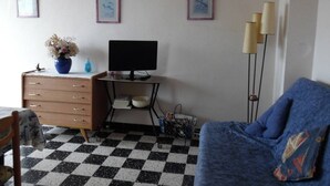 Een kamer met een geruite vloer, een bureau met een computer, een blauwe bank en drie ingelijste foto's aan de muur.