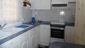 Een keuken met witte kasten, een fornuis, een gootsteen en een raam met gordijn.