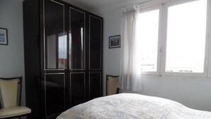 Een slaapkamer met een bed, een kledingkast, twee stoelen, een zwart-wit geruite vloer en een raam met gordijnen.