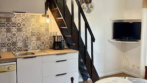 Una cocina compacta con baldosas estampadas, una cafetera y un televisor montado en la pared.